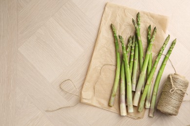 Photo of Fresh green asparagus stems and thread on wooden table, flat lay. Space for text