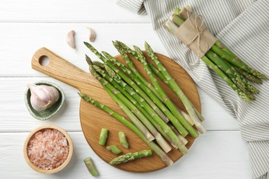 Fresh green asparagus stems, garlic and sea salt on white wooden table, flat lay