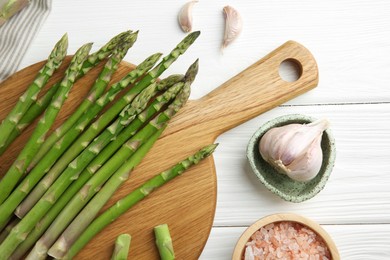 Fresh green asparagus stems, garlic and sea salt on white wooden table, flat lay