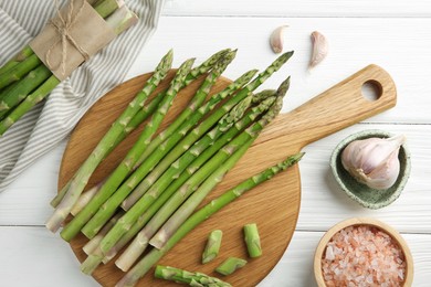 Fresh green asparagus stems, garlic and sea salt on white wooden table, flat lay