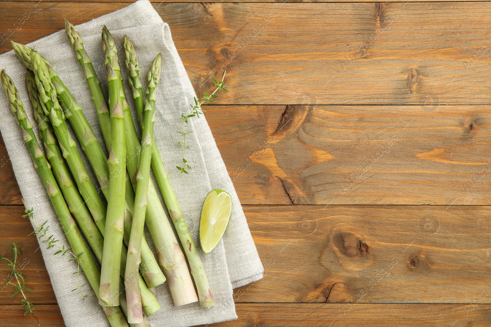 Photo of Fresh green asparagus stems and lime on wooden table, top view. Space for text