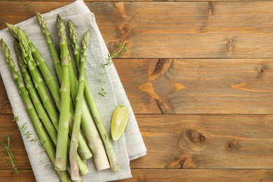 Photo of Fresh green asparagus stems and lime on wooden table, top view. Space for text