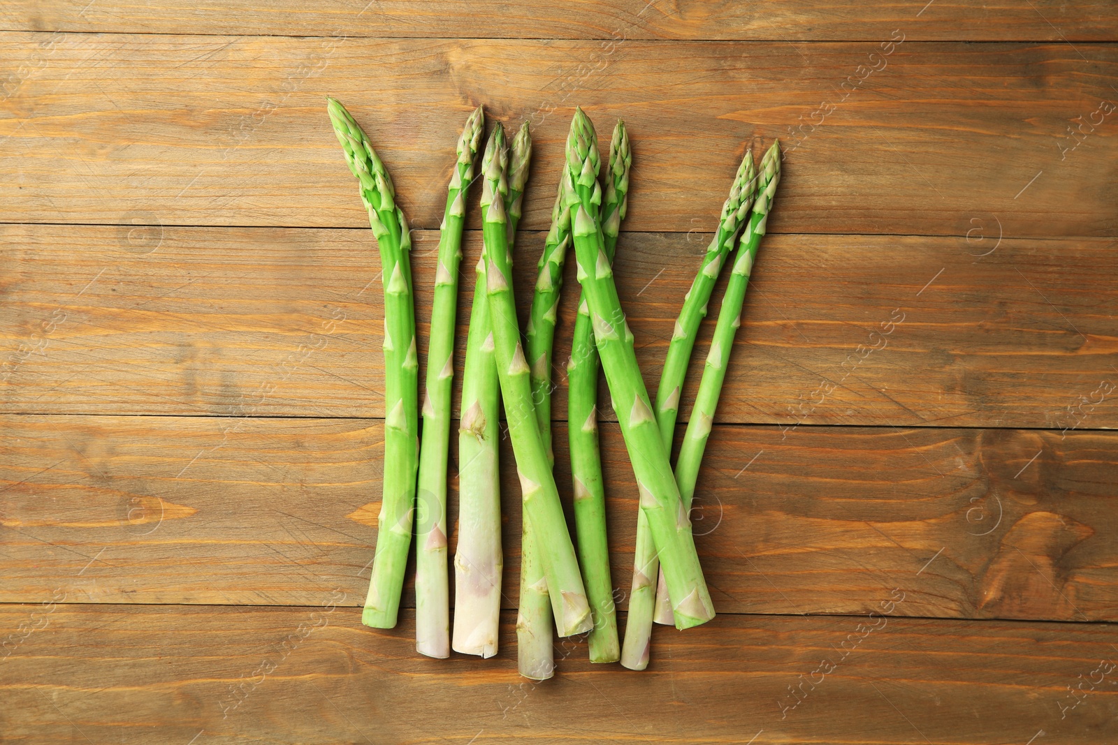 Photo of Fresh green asparagus stems on wooden table, top view