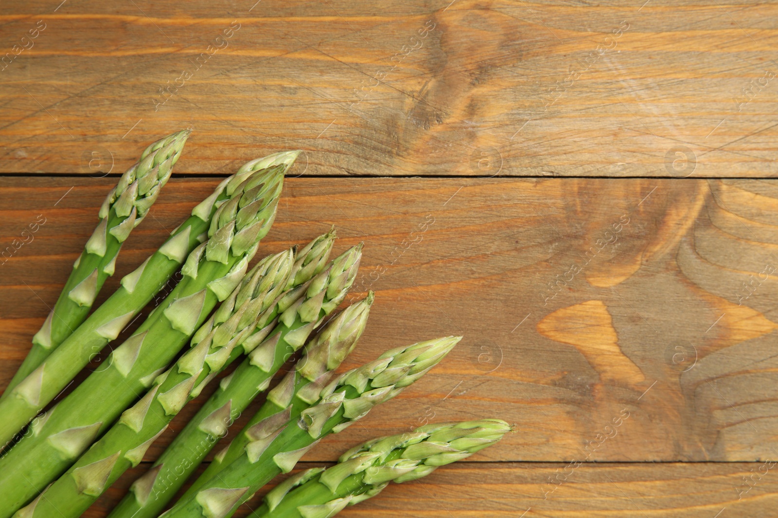 Photo of Fresh green asparagus stems on wooden table, top view. Space for text