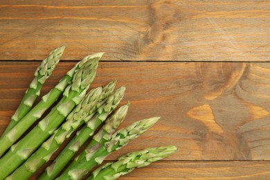 Photo of Fresh green asparagus stems on wooden table, top view. Space for text