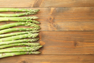 Photo of Fresh green asparagus stems on wooden table, top view. Space for text