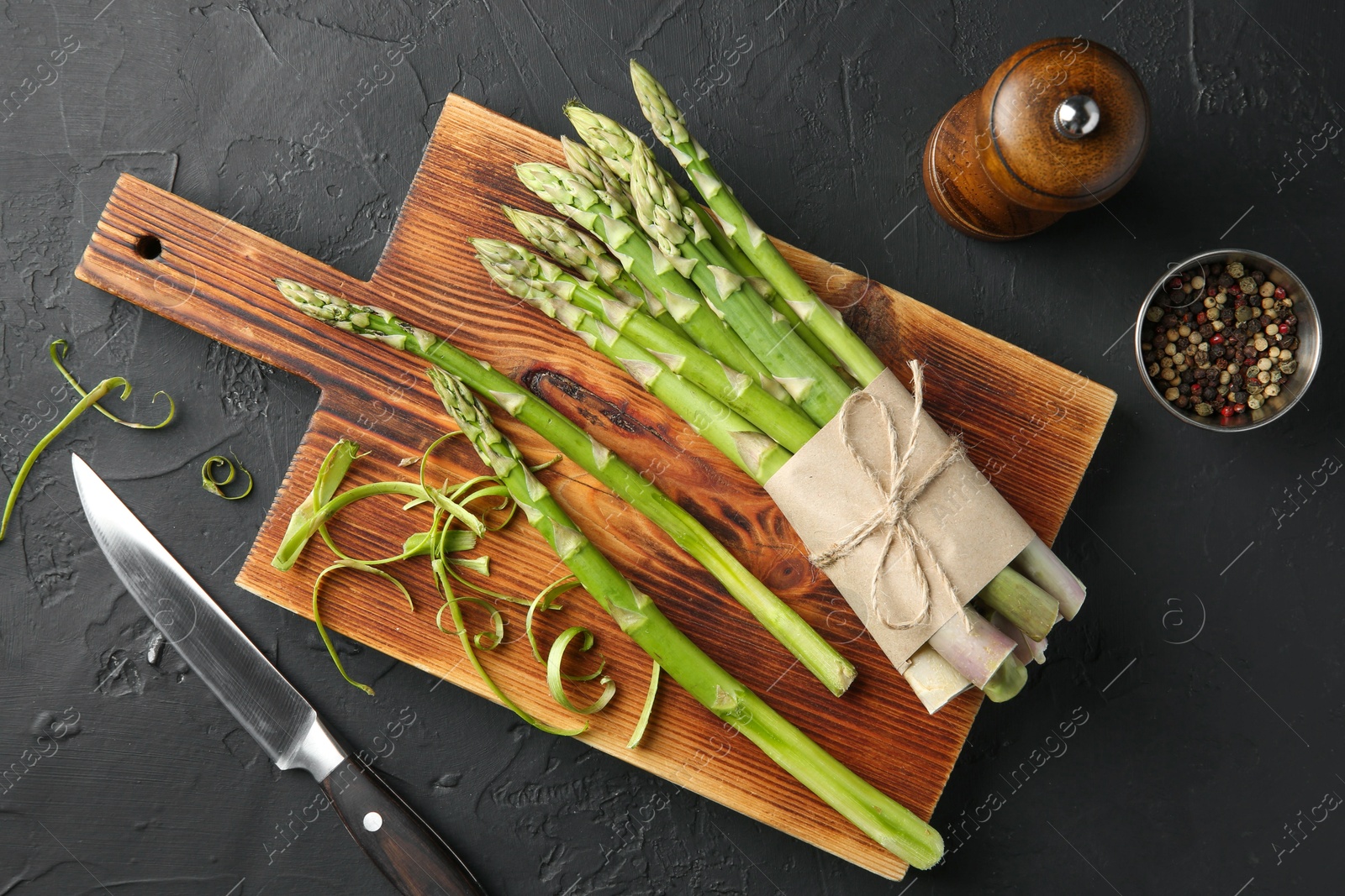 Photo of Fresh green asparagus stems, spices and knife on gray textured table, flat lay