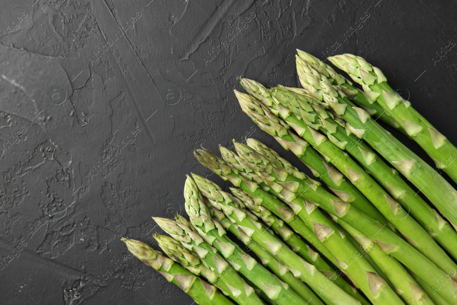 Photo of Fresh green asparagus stems on gray textured table, top view. Space for text