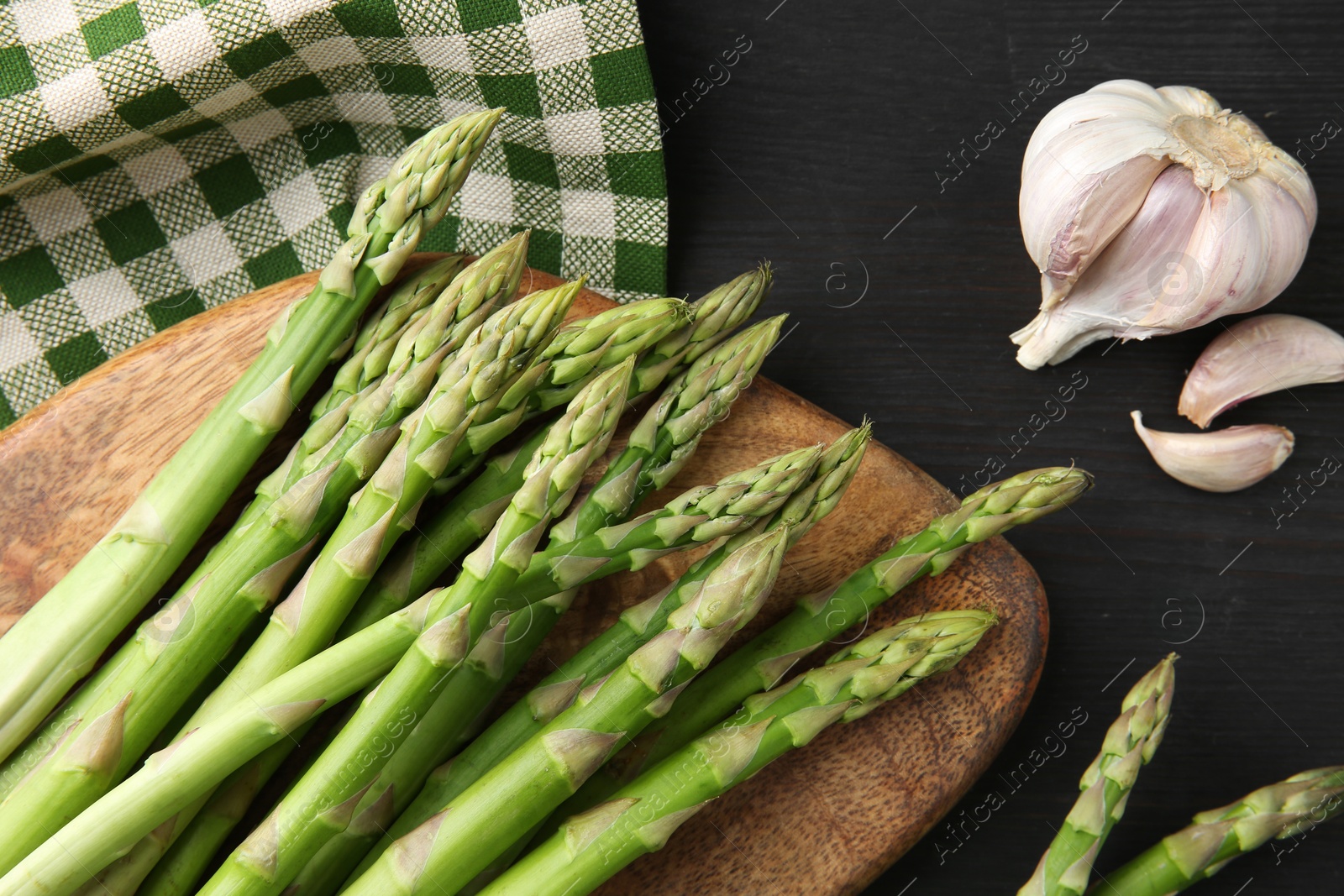 Photo of Fresh green asparagus stems and garlic on gray wooden table, flat lay