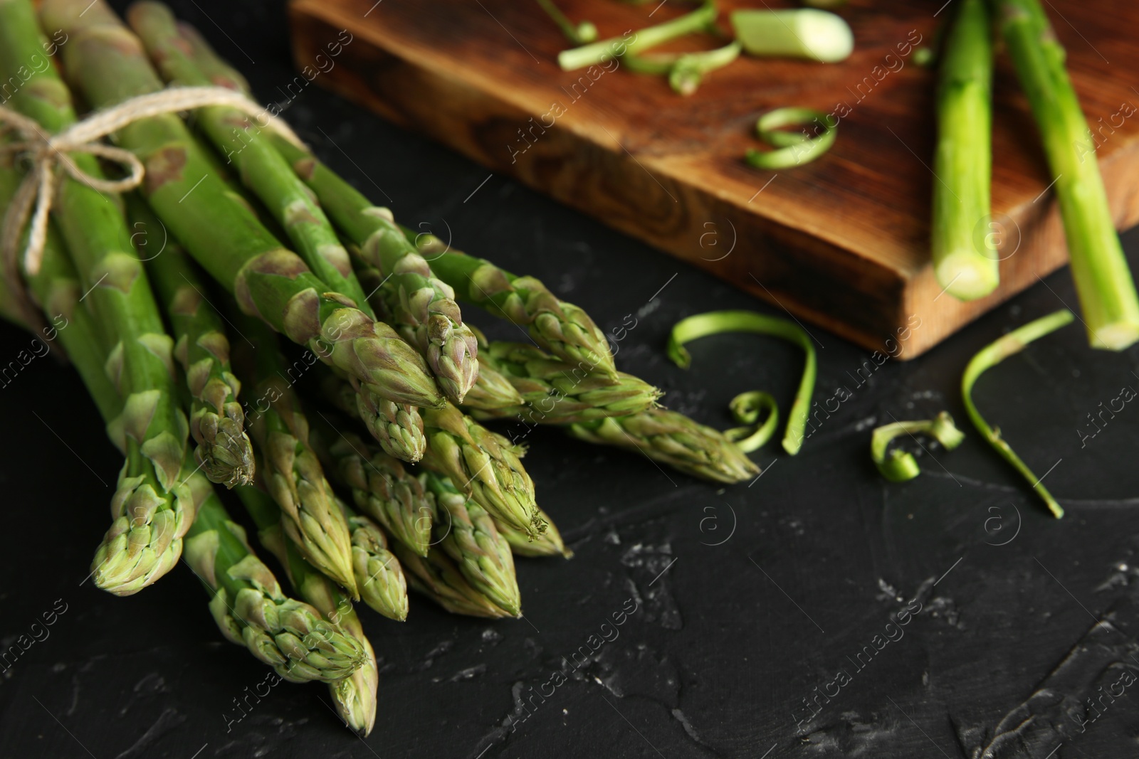 Photo of Fresh green asparagus stems on black textured table, closeup