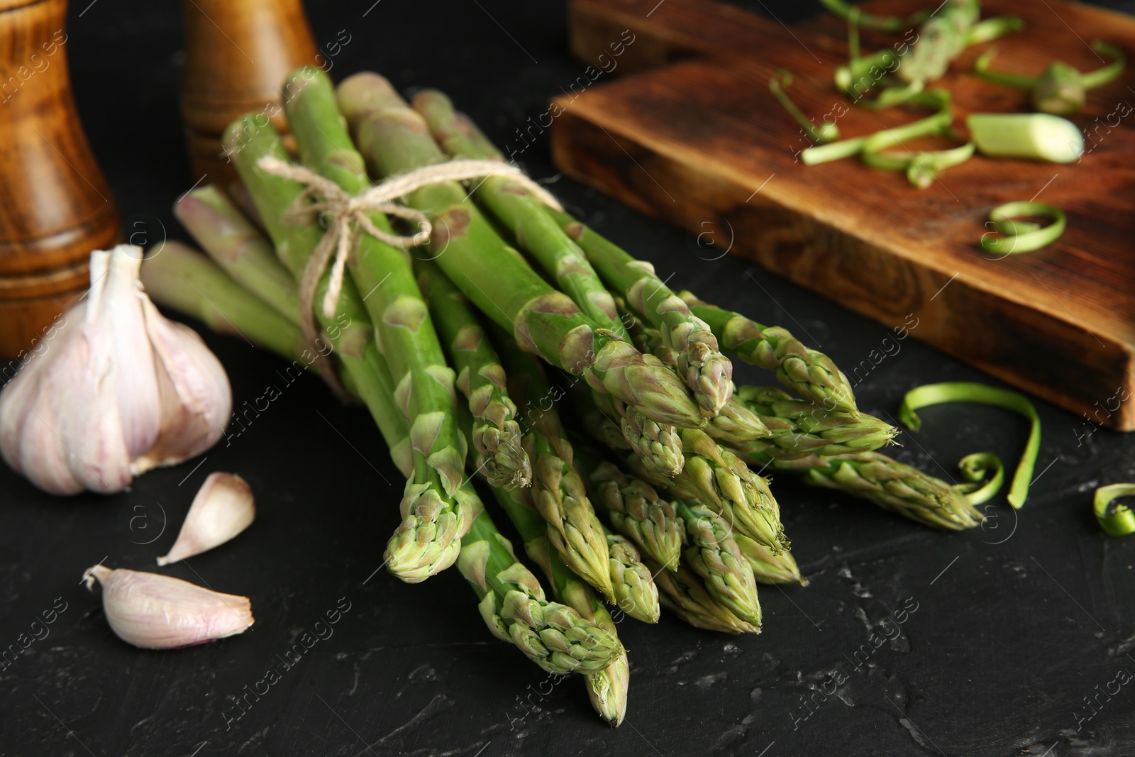 Photo of Fresh green asparagus stems and garlic on black textured table, closeup