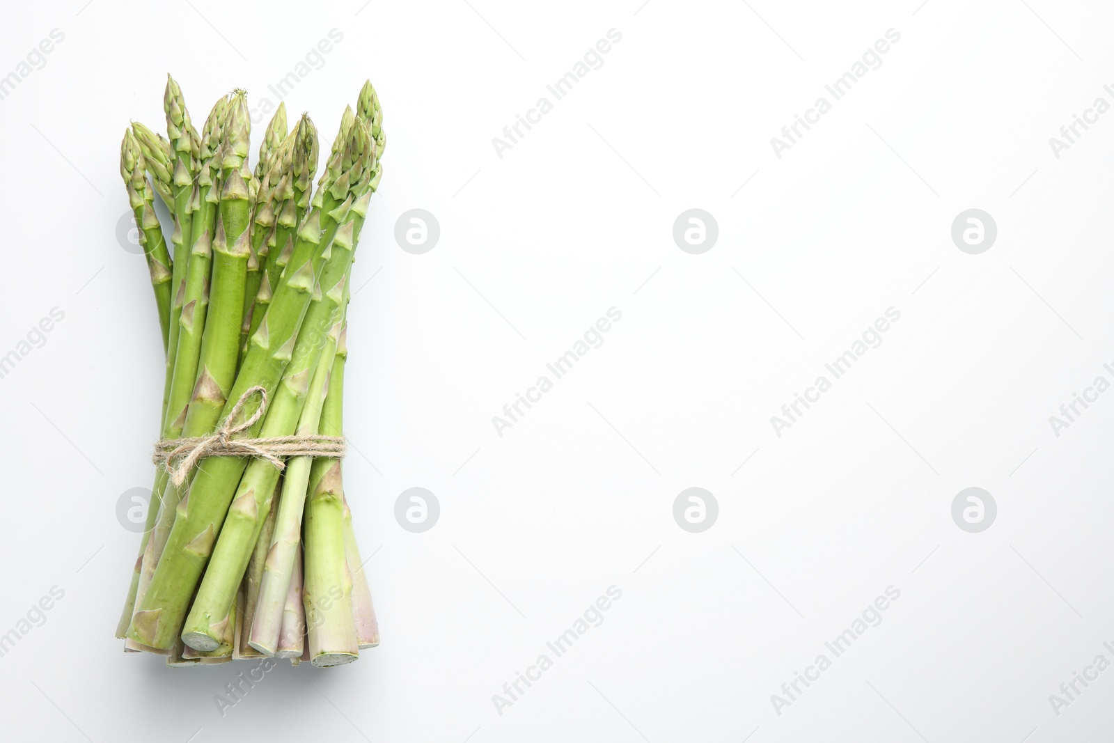 Photo of Bunch of fresh green asparagus stems on white table, top view. Space for text