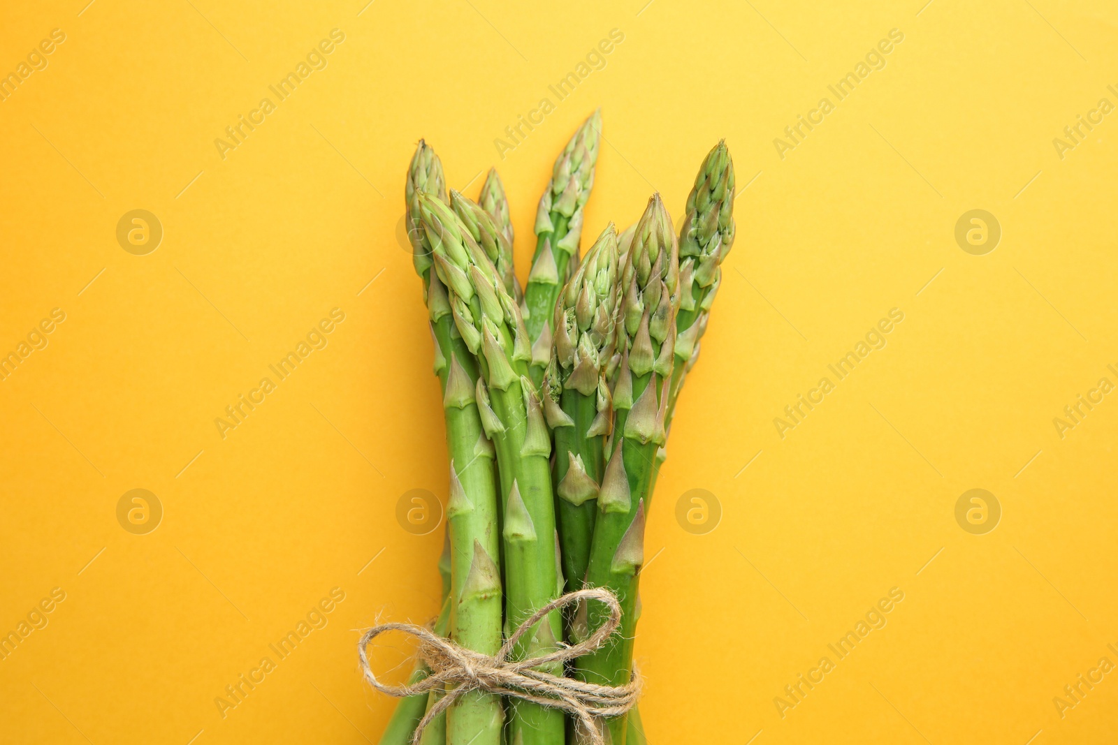 Photo of Fresh green asparagus stems on orange table, top view