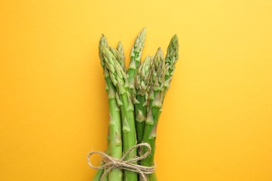 Photo of Fresh green asparagus stems on orange table, top view