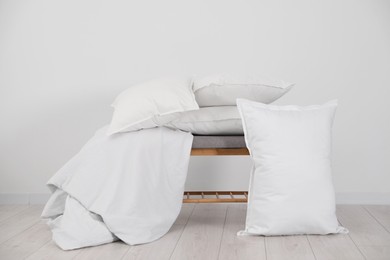 Clean pillows, blanket and storage bench on floor near white wall