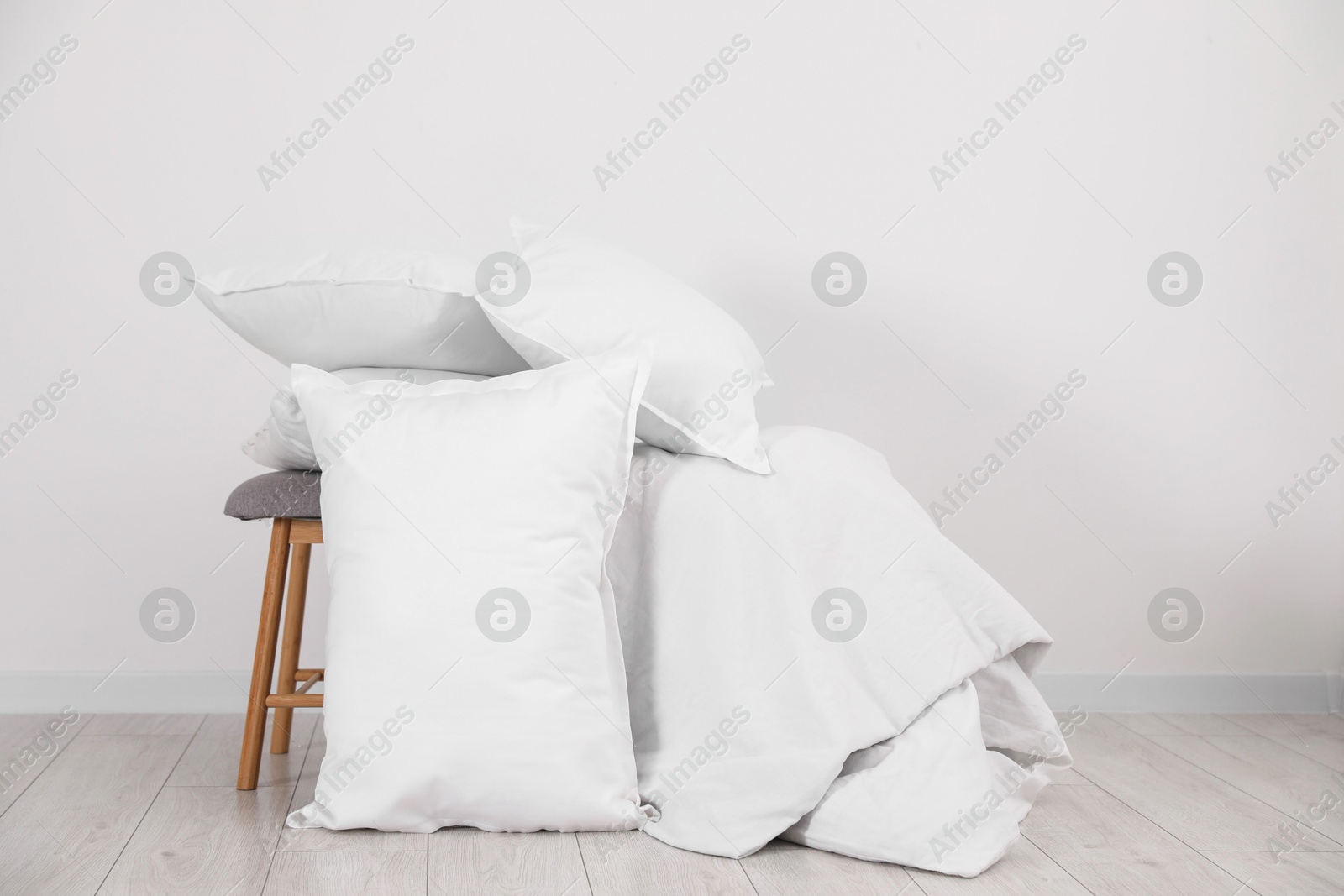 Photo of Clean pillows, blanket and stool on floor near white wall