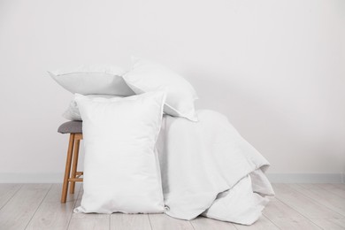 Photo of Clean pillows, blanket and stool on floor near white wall