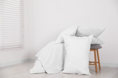 Photo of Clean pillows, blanket and stool on floor near white wall. Space for text