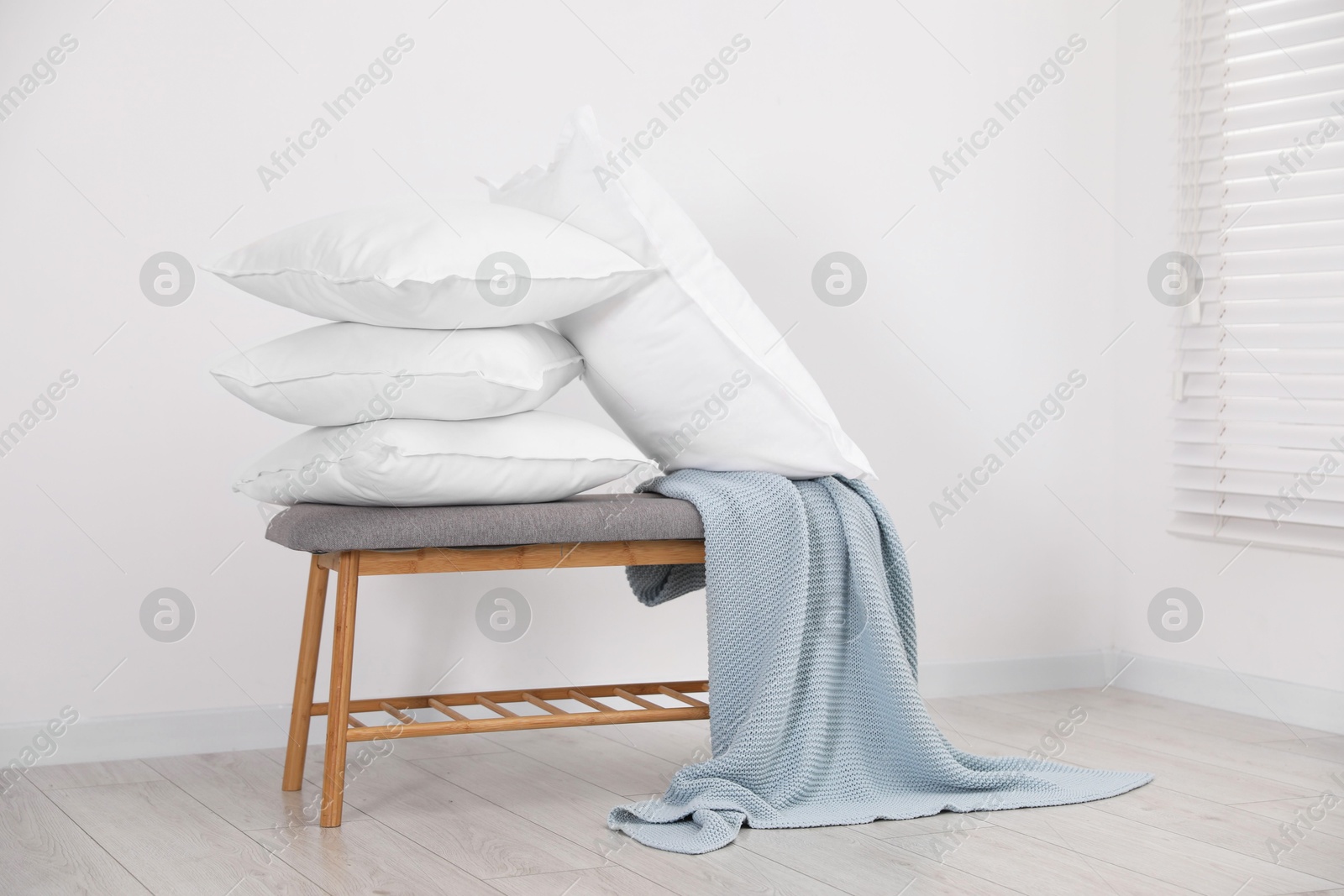 Photo of Clean pillows, blanket and storage bench on floor near white wall