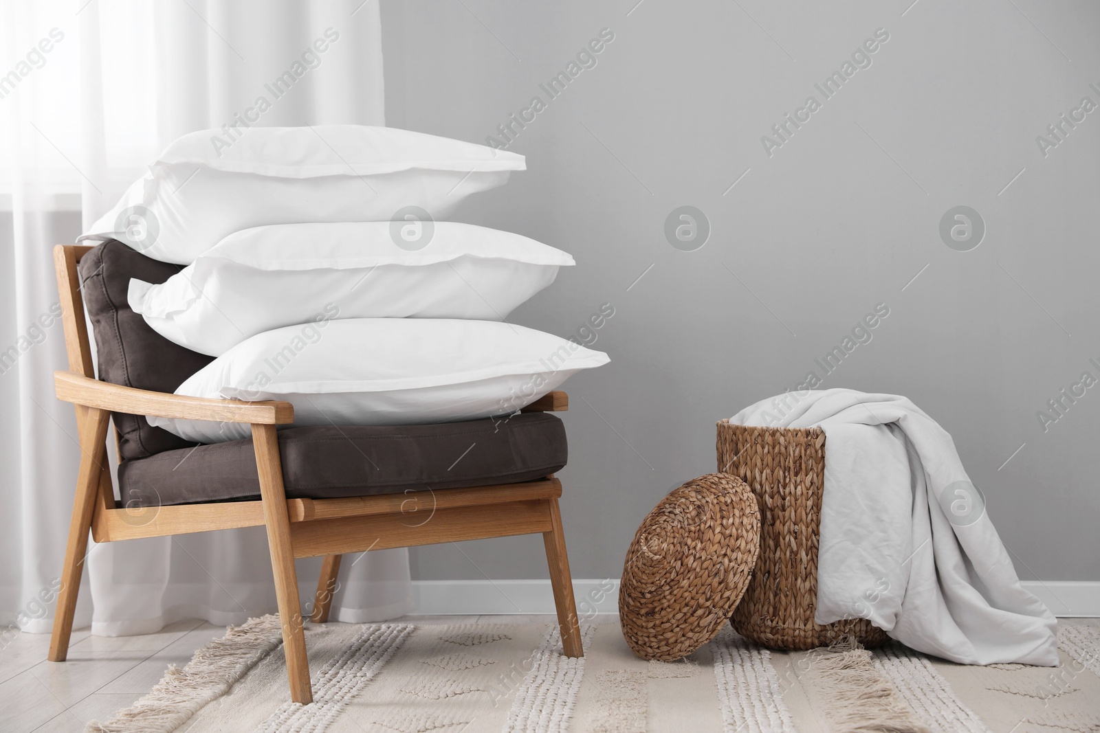 Photo of Stack of white pillows, armchair and wicker basket on floor indoors