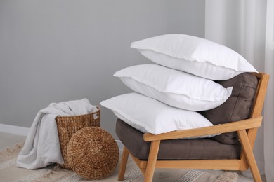 Stack of white pillows, armchair and wicker basket on floor indoors