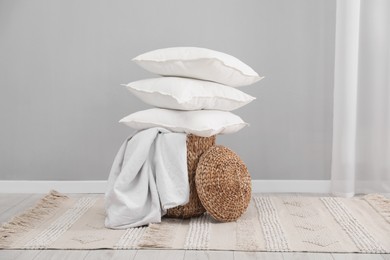 Stack of white pillows, blanket and wicker basket on floor indoors