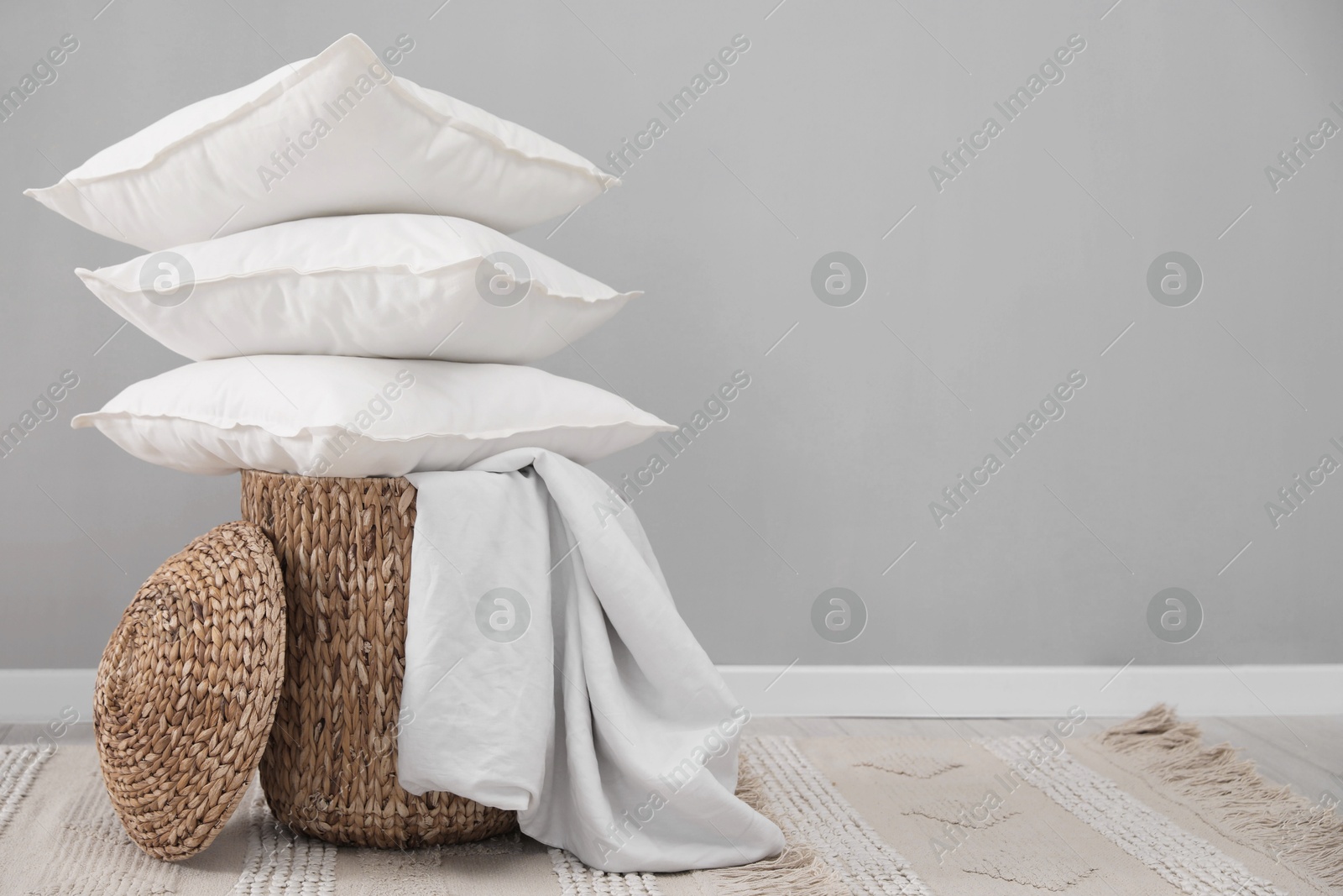 Photo of Stack of white pillows, blanket and wicker basket on floor indoors. Space for text