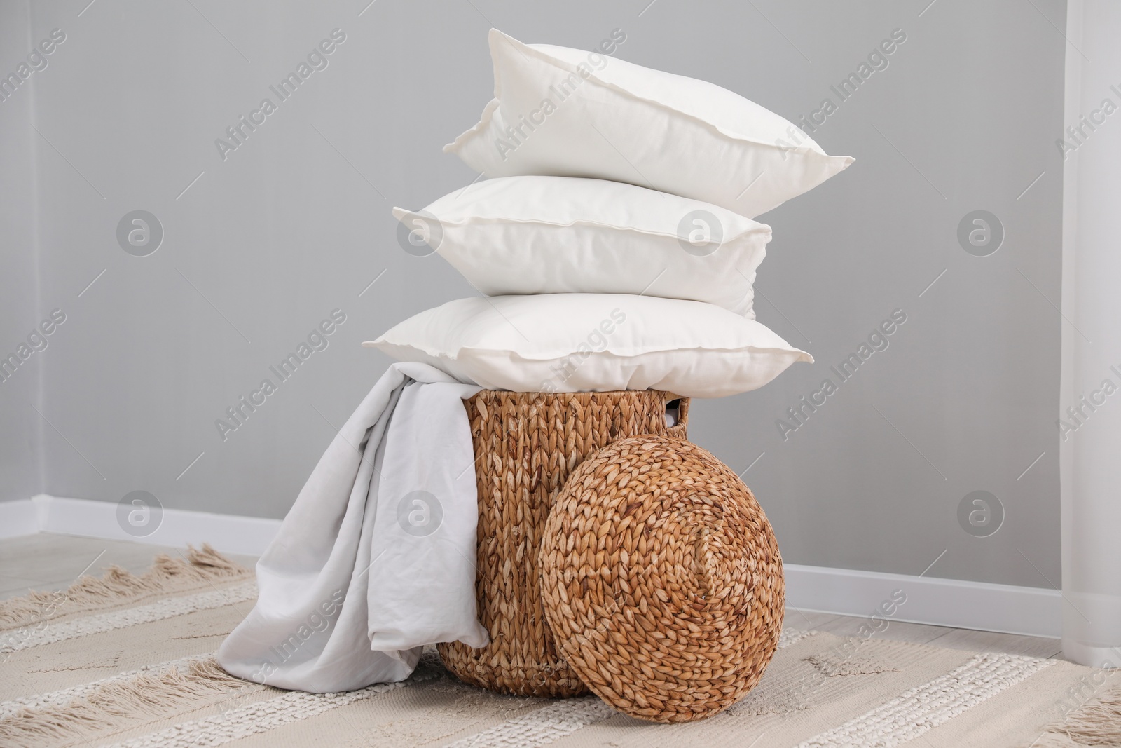 Photo of Stack of white pillows, blanket and wicker basket on floor indoors