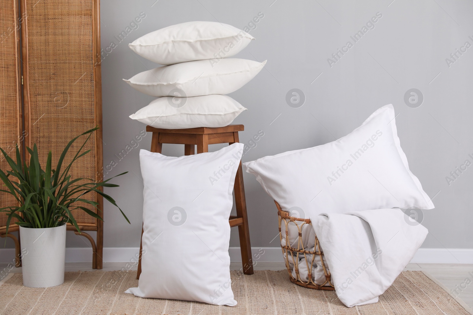 Photo of Stack of pillows, stool, storage basket and houseplant on floor indoors