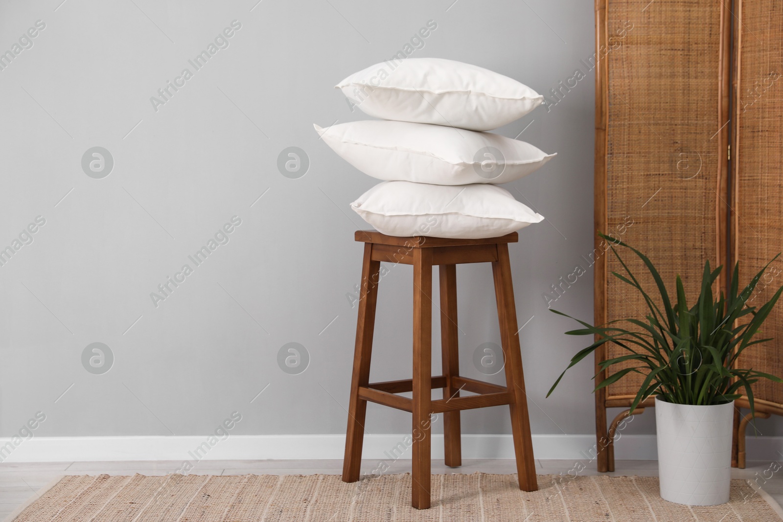 Photo of Stack of pillows, stool and houseplant on floor indoors. Space for text