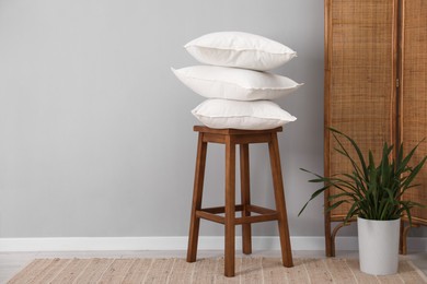 Stack of pillows, stool and houseplant on floor indoors. Space for text