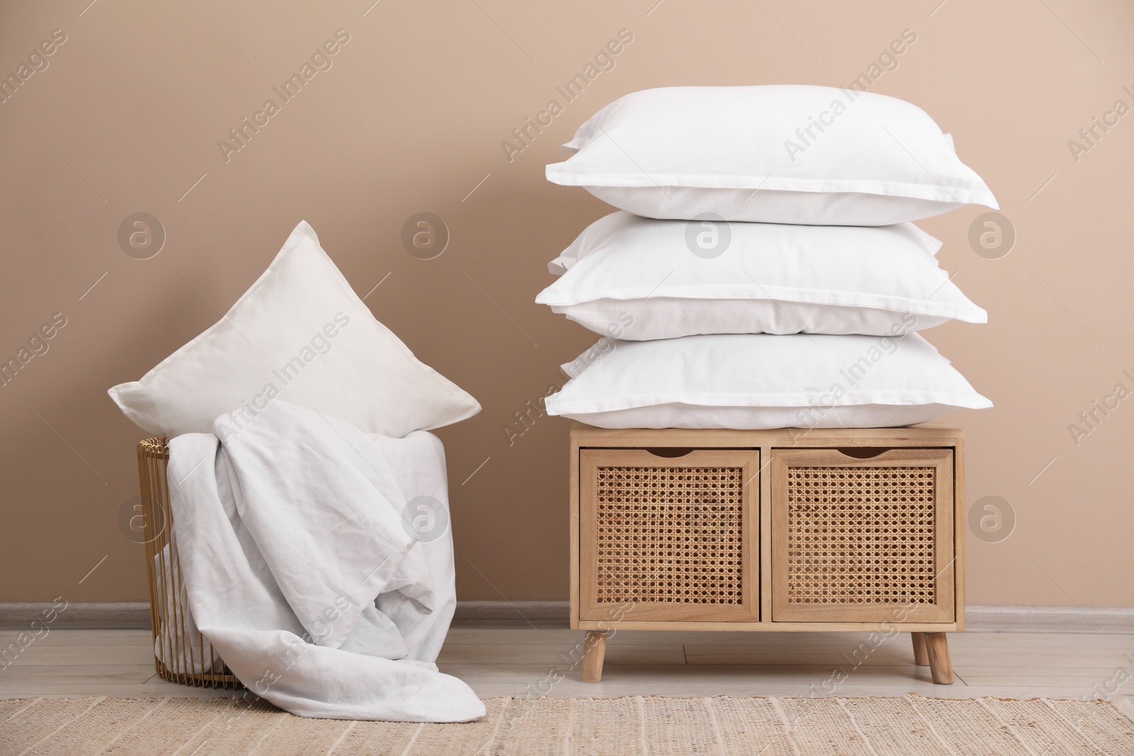 Photo of Stack of pillows, storage cabinet, basket and blanket near beige wall