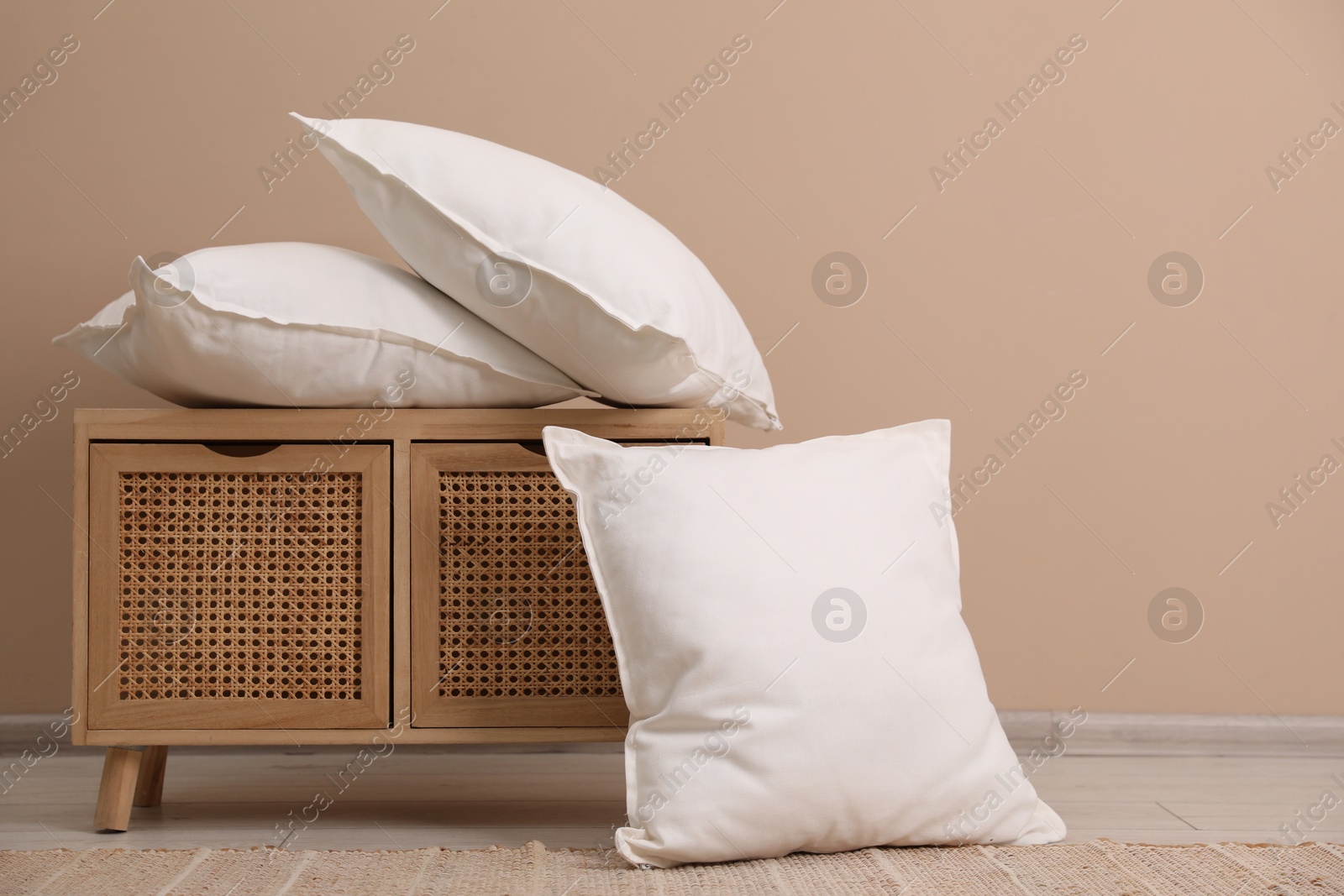 Photo of Soft pillows and storage cabinet on floor near beige wall