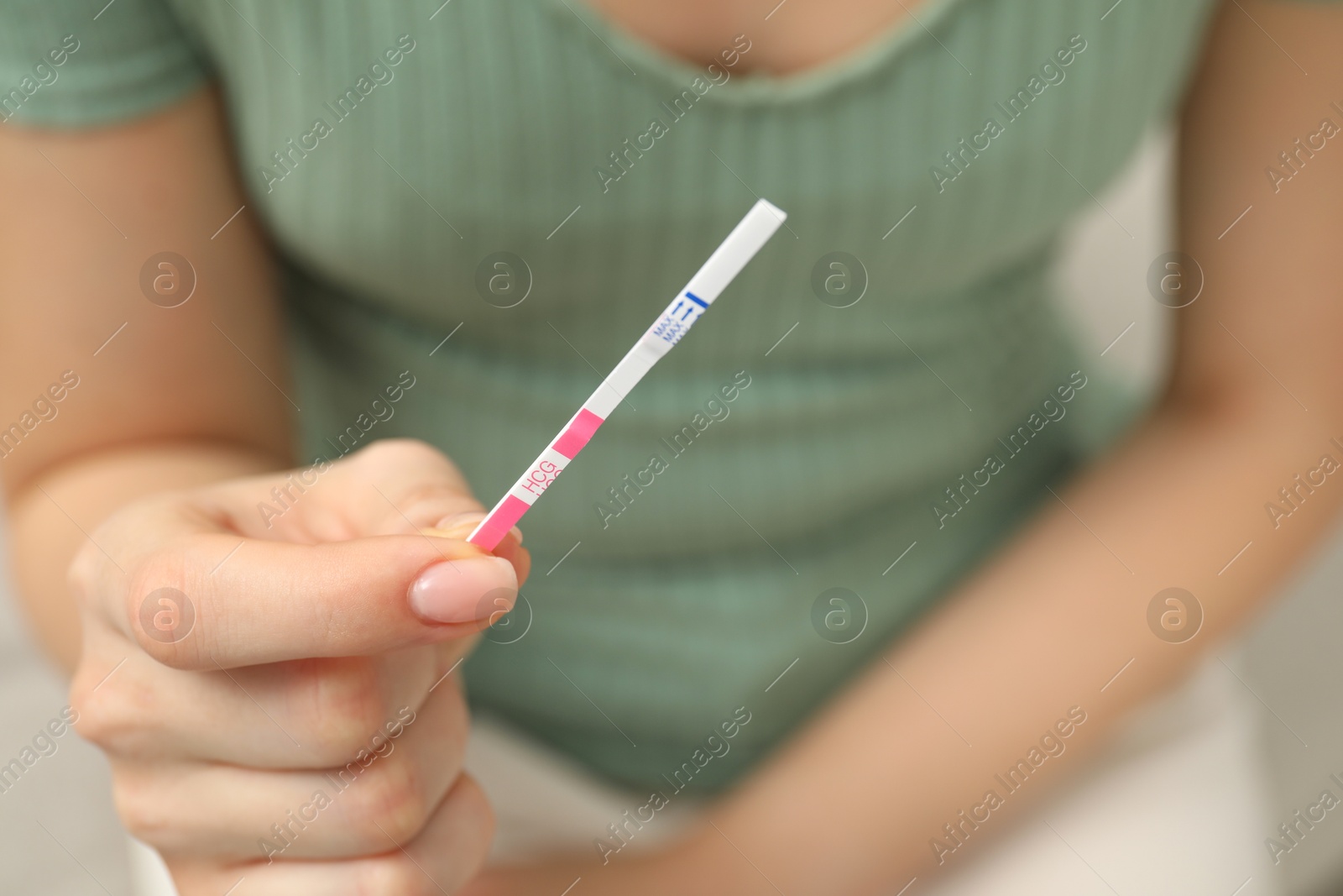 Photo of Woman holding pregnancy test indoors, closeup view