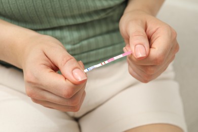 Photo of Woman holding positive pregnancy test indoors, closeup view