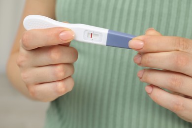 Woman holding negative pregnancy test indoors, closeup view