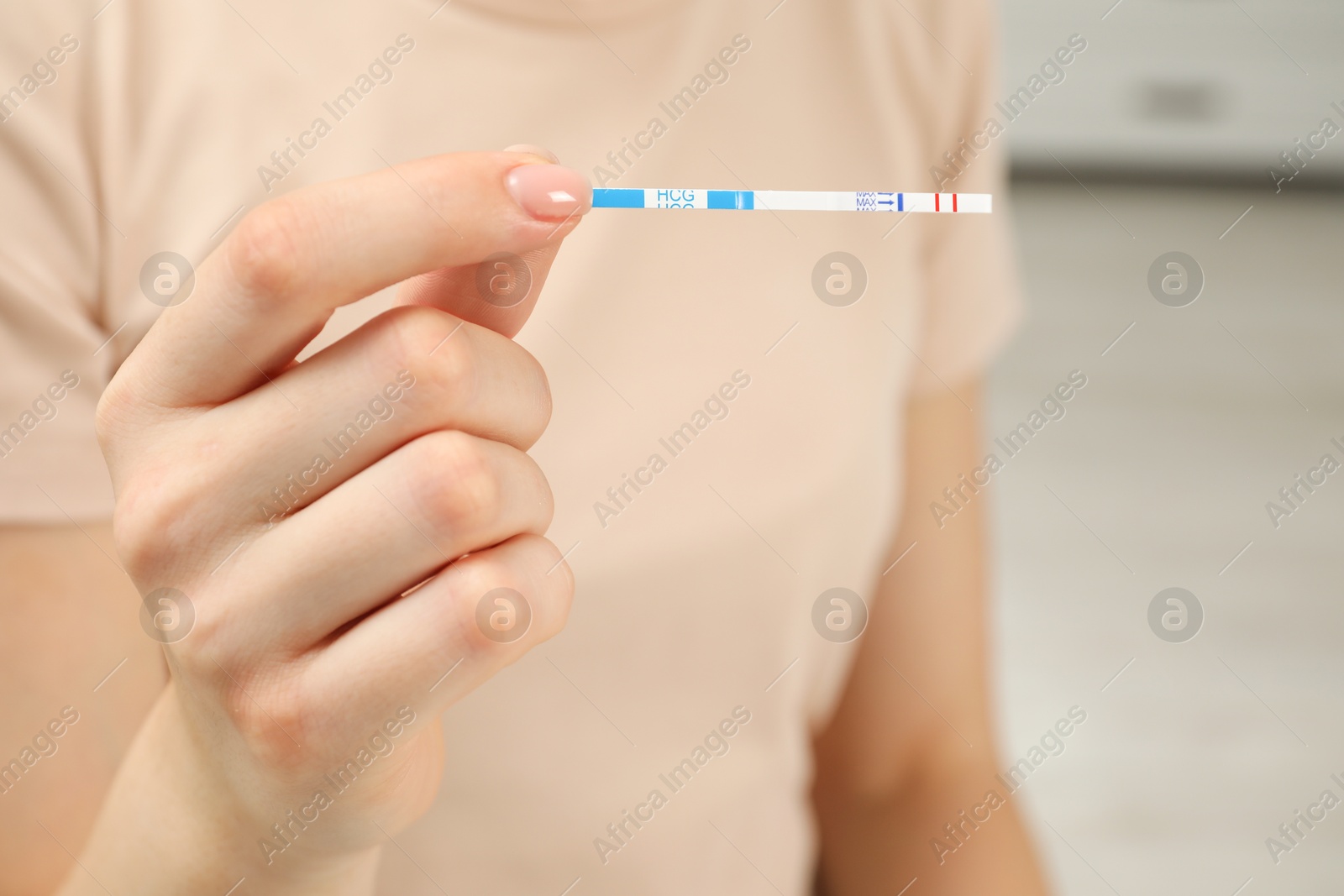 Photo of Woman holding positive pregnancy test indoors, closeup view