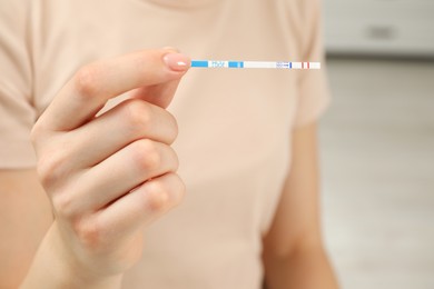 Woman holding positive pregnancy test indoors, closeup view