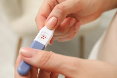 Photo of Woman holding positive pregnancy test indoors, closeup view