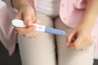 Photo of Woman holding positive pregnancy test indoors, closeup view