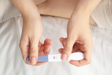 Woman holding positive pregnancy test indoors, closeup view