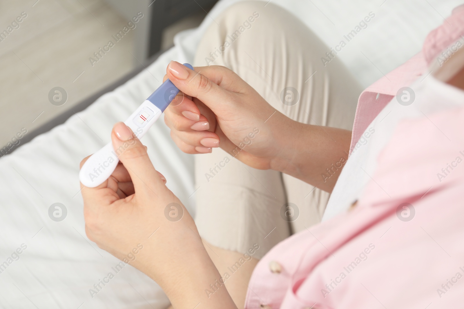 Photo of Woman holding positive pregnancy test indoors, closeup view