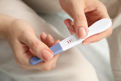 Woman holding positive pregnancy test indoors, closeup view