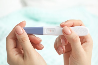 Woman holding positive pregnancy test indoors, closeup view