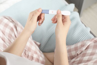 Woman holding positive pregnancy test indoors, closeup view