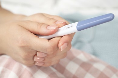 Woman holding pregnancy test indoors, closeup view