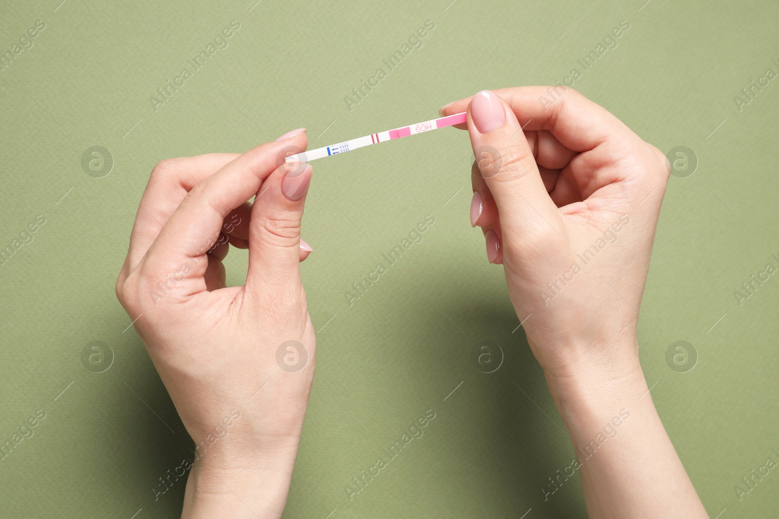 Photo of Woman holding pregnancy test on olive background, top view