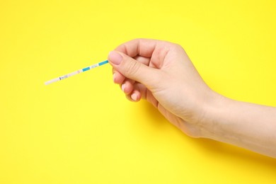 Photo of Woman holding pregnancy test on yellow background, closeup