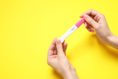 Photo of Woman holding pregnancy test on yellow background, closeup. Space for text