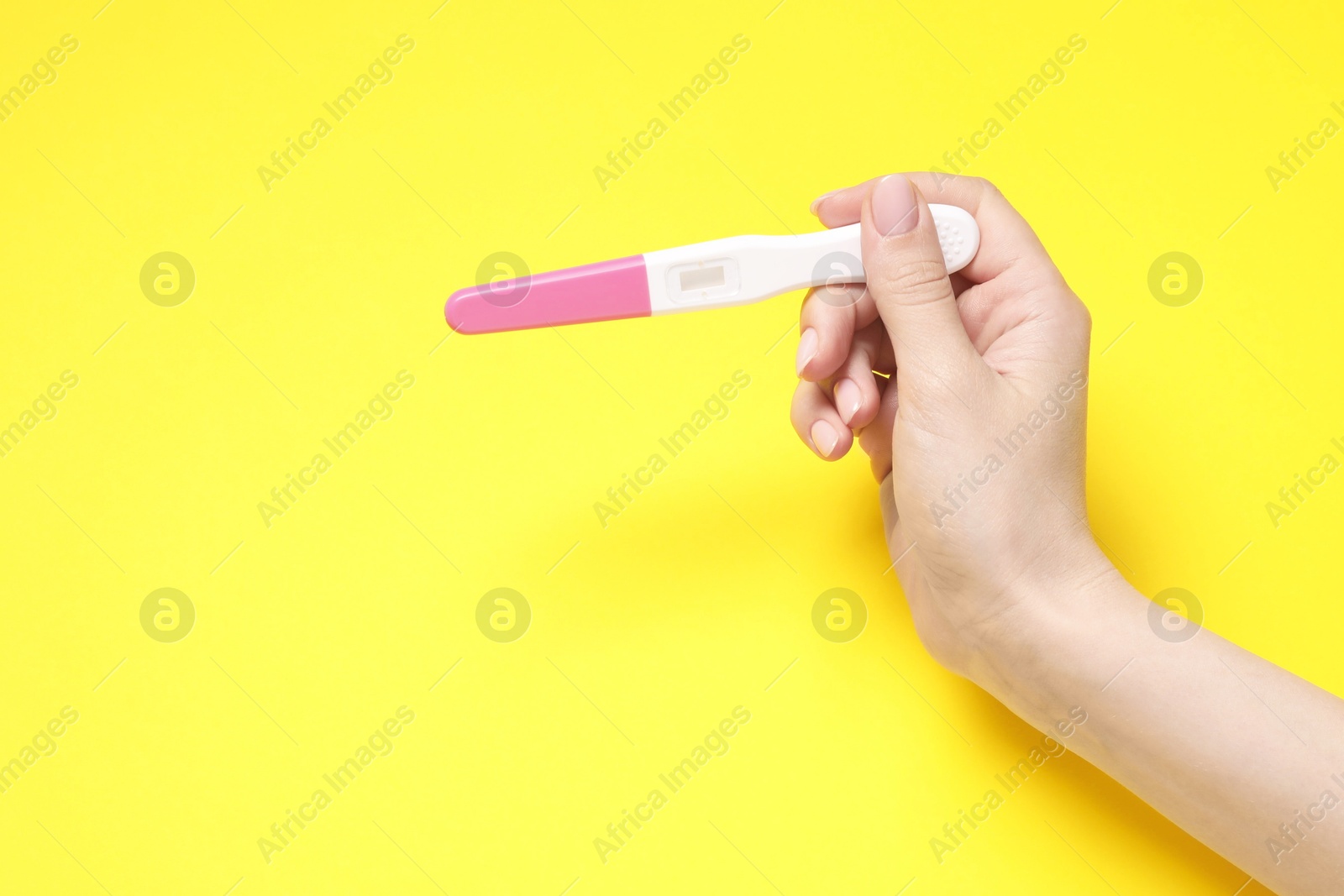 Photo of Woman holding pregnancy test on yellow background, closeup. Space for text